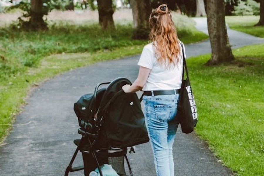 En bild på en kvinna med barnvagn på promenad omgiven av lite träd. bilden symboliserar hälsa.